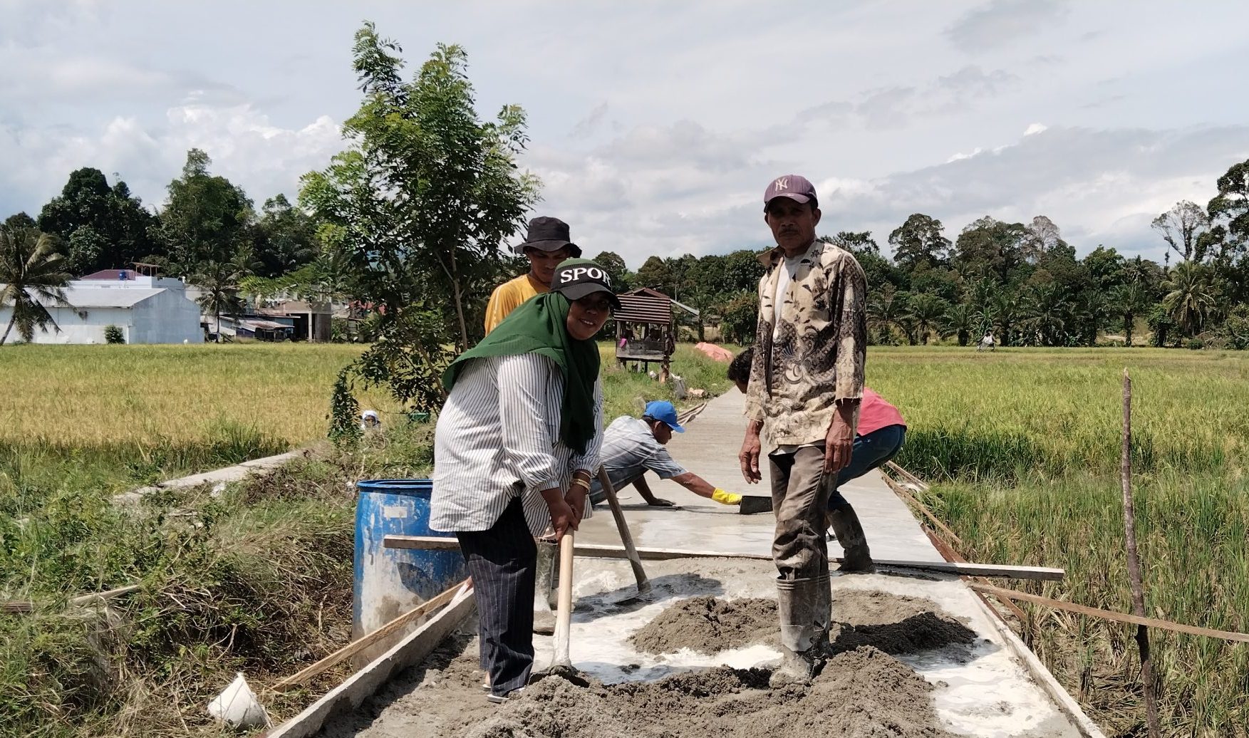 Foto : Kepala Desa Sorkam Tengah, Rahmayani Hutagalung Tampak memegang cangkul membantu mengerjakan jalan rapat beton.